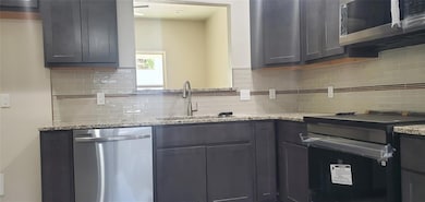 Kitchen featuring stainless steel appliances, tasteful backsplash, and light stone counters