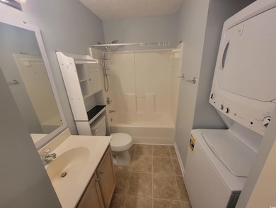 Bathroom with stacked washer and clothes dryer, vanity, toilet,  shower combination, and tile patterned floors