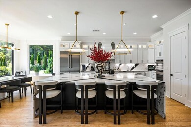 Kitchen with dark cabinets, light wood-style flooring, glass insert cabinets, light stone counters, and recessed lighting