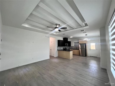 Kitchen featuring open floor plan, stainless steel appliances, a raised ceiling, dark countertops, and wood finished floors