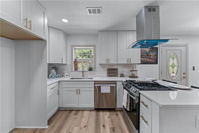 Kitchen featuring appliances with stainless steel finishes, a sink, island range hood, light wood-style floors, and light countertops
