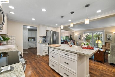 Kitchen featuring open floor plan, white cabinetry, dark wood finished floors, ornamental molding, and decorative light fixtures