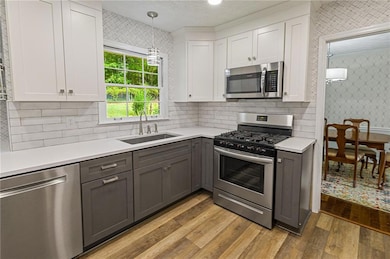 Kitchen featuring wallpapered walls, white cabinets, appliances with stainless steel finishes, dark wood-style floors, and hanging light fixtures