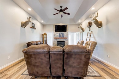 Living area featuring a ceiling fan, baseboards, a stone fireplace, light wood-style flooring, and recessed lighting