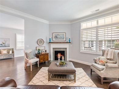 Living room with crown molding, a fireplace with flush hearth, and dark wood finished floors