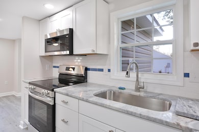 Kitchen with appliances with stainless steel finishes, white cabinetry, light stone counters, backsplash, and plenty of natural light