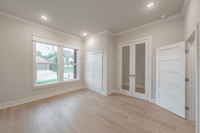 Unfurnished bedroom featuring french doors, ornamental molding, light wood-style floors, recessed lighting, and a closet