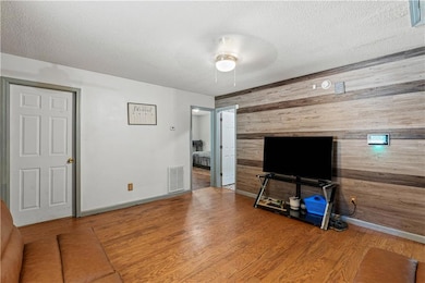 Unfurnished living room featuring wood walls, wood finished floors, a textured ceiling, ceiling fan, and an accent wall