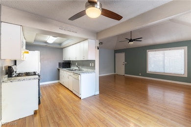 Kitchen featuring white appliances, white cabinetry, a textured ceiling, light wood-style flooring, and open floor plan
