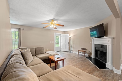Living room with a fireplace, ceiling fan, a textured ceiling, and wood finished floors