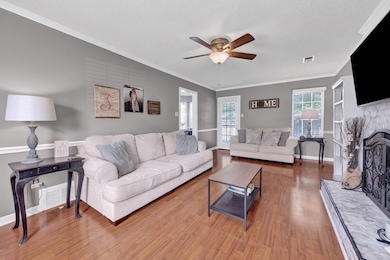 Living area featuring ceiling fan, wood finished floors, ornamental molding, baseboards, and a brick fireplace