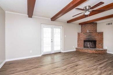 Unfurnished living room featuring beamed ceiling, a ceiling fan, wood finished floors, a brick fireplace, and baseboards