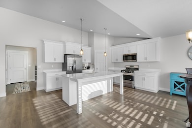 Kitchen featuring appliances with stainless steel finishes, white cabinetry, a kitchen island with sink, a kitchen bar, and dark wood-type flooring