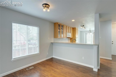 Kitchen with white appliances, glass insert cabinets, dark wood-style floors, light countertops, and a peninsula
