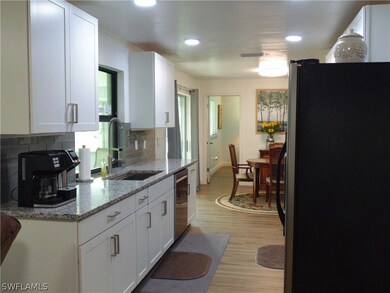 Kitchen with tasteful backsplash, white cabinetry, light wood-type flooring, appliances with stainless steel finishes, and sink