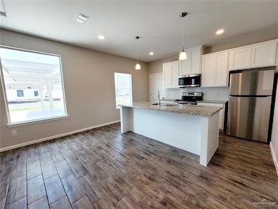 Kitchen featuring appliances with stainless steel finishes, white cabinetry, tasteful backsplash, light stone counters, and hanging light fixtures