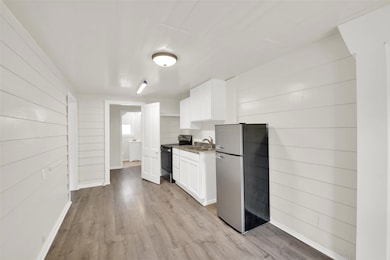 Kitchen featuring appliances with stainless steel finishes, white cabinets, light wood-style flooring, wood walls, and light countertops