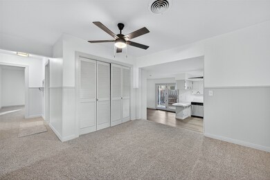 Unfurnished living room featuring light carpet, wainscoting, and ceiling fan