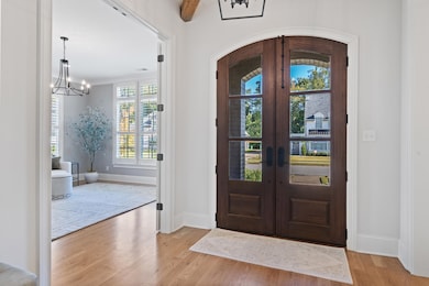 Entrance foyer with a chandelier, french doors, light wood finished floors, and ornamental molding