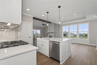 Kitchen featuring white cabinets, an island with sink, stainless steel dishwasher, a tray ceiling, and ornamental molding