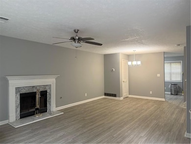 Unfurnished living room with wood finished floors, a textured ceiling, a premium fireplace, ceiling fan, and a chandelier