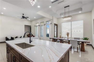 Kitchen featuring dark brown cabinetry, light tile patterned flooring, light stone counters, a tray ceiling, and a center island with sink