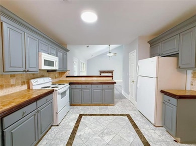 Kitchen with gray cabinetry, decorative backsplash, inlaid floor details, white appliances, and lofted ceiling