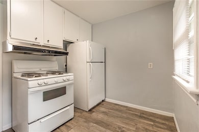 Kitchen featuring white appliances, under cabinet range hood, white cabinetry, and light wood finished floors