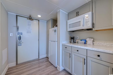 Kitchen featuring light wood-style flooring, baseboards, gray cabinetry, white appliances, and light stone counters