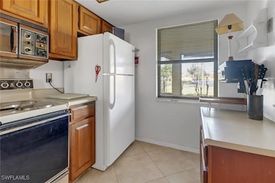 Kitchen featuring hanging light fixtures, light tile patterned floors, white refrigerator, and electric stove