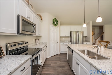Kitchen with appliances with stainless steel finishes, dark wood-style flooring, decorative light fixtures, and light stone counters