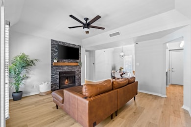 Living room with light wood-type flooring, ceiling fan, a stone fireplace, and a chandelier