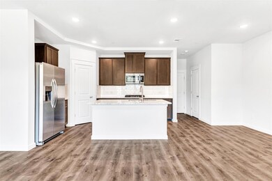 Kitchen featuring a center island with sink, light stone counters, backsplash, hardwood / wood-style flooring, and appliances with stainless steel finishes