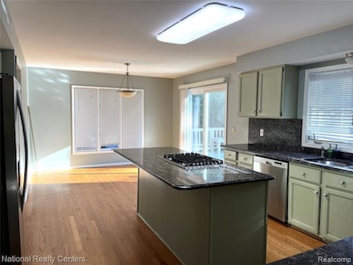 Kitchen with green cabinets, dark stone counters, and light wood-style floors