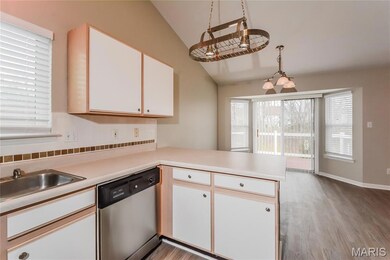 Kitchen featuring a peninsula, white cabinetry, light countertops, stainless steel dishwasher, and vaulted ceiling