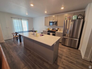 Kitchen featuring stainless steel appliances, dark laminate flooring, light countertops, gray cabinetry, and recessed lighting