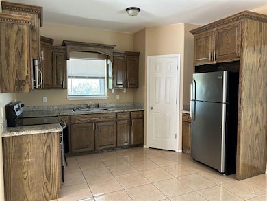 Kitchen featuring appliances with stainless steel finishes, light tile patterned floors, and light stone countertops