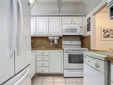 Kitchen featuring white appliances, light tile patterned floors, white cabinets, and dark countertops
