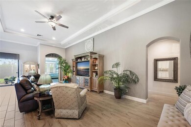 Living room featuring a tray ceiling, arched walkways, a ceiling fan, light wood-type flooring, and baseboards