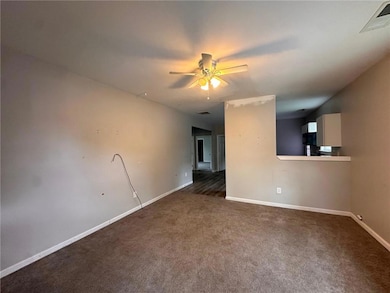Empty room featuring dark carpet, a ceiling fan, and baseboards