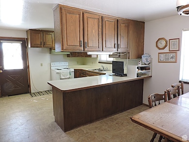 Kitchen with a peninsula, light countertops, white electric stove, brown cabinets, and light floors