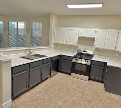 Kitchen with appliances with stainless steel finishes, white cabinetry, a peninsula, light countertops, and gray cabinets
