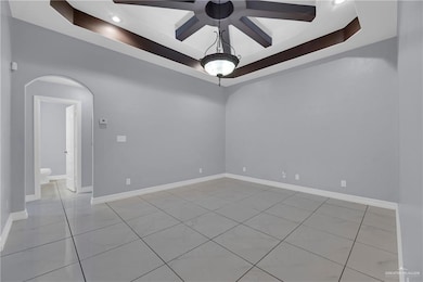 Empty room with arched walkways, light tile patterned floors, baseboards, a raised ceiling, and recessed lighting