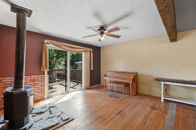 Living room with a wood stove, wood-type flooring, wood walls, a textured ceiling, and beam ceiling