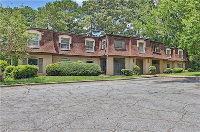 Front of property featuring mansard roof, stucco siding, uncovered parking, and a shingled roof