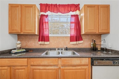 Kitchen featuring white dishwasher, a sink, dark countertops, and backsplash