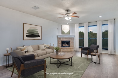 Living room with wood finished floors, a fireplace, ceiling fan, and a textured ceiling