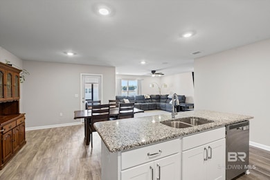 Kitchen with stainless steel dishwasher, light wood-style flooring, a center island with sink, light stone countertops, and recessed lighting