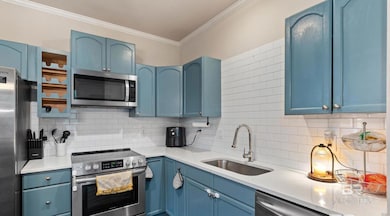 Kitchen with blue cabinetry, stainless steel appliances, ornamental molding, tasteful backsplash, and light stone counters
