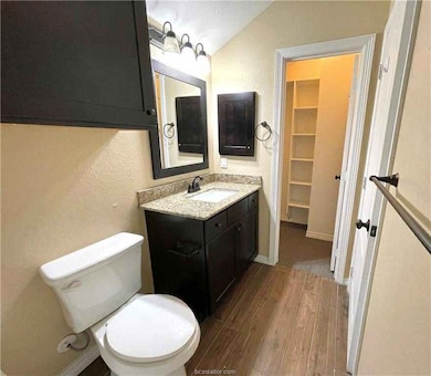 Half bath with wood finished floors, vanity, vaulted ceiling, a textured wall, and a walk in closet